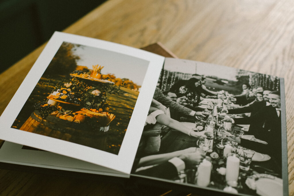an open wedding album with a picture of a long table with happy people toasting